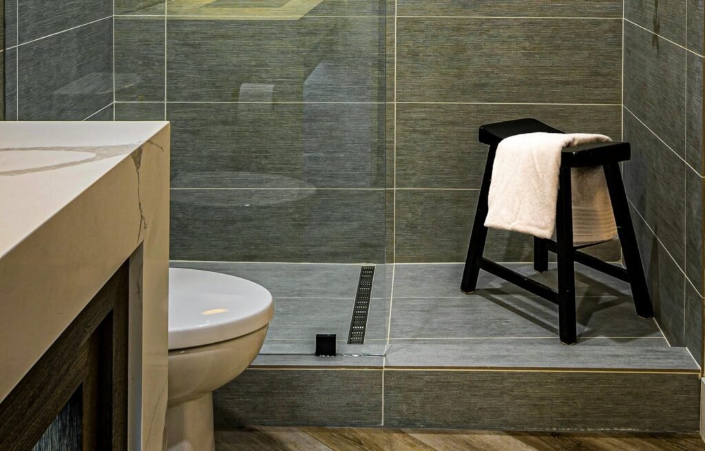 Stylish bathroom featuring a glass shower enclosure, stool with towel, and modern fixtures.