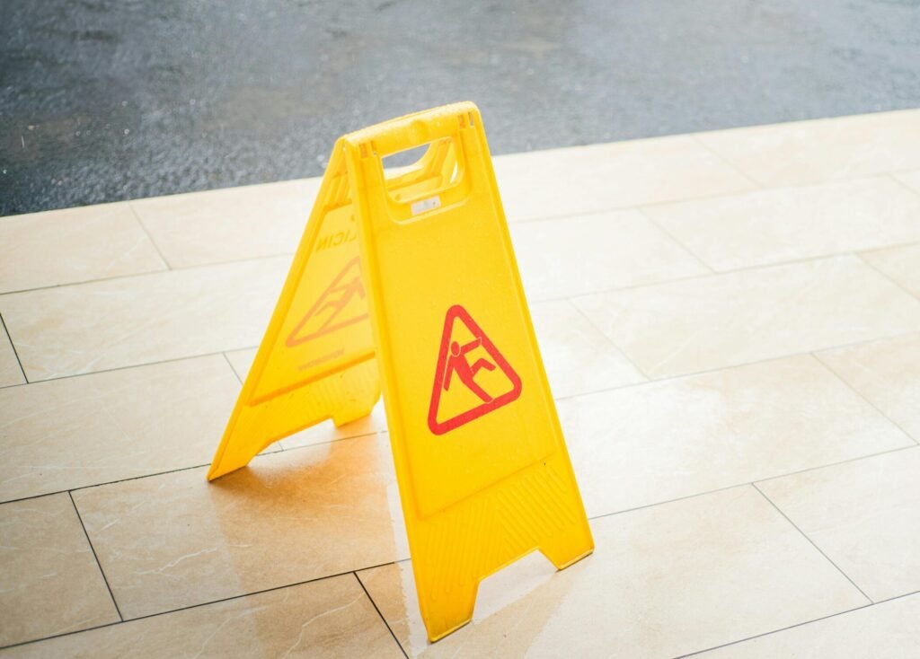 A bright yellow caution sign placed on a tile floor indicating a wet area for safety.